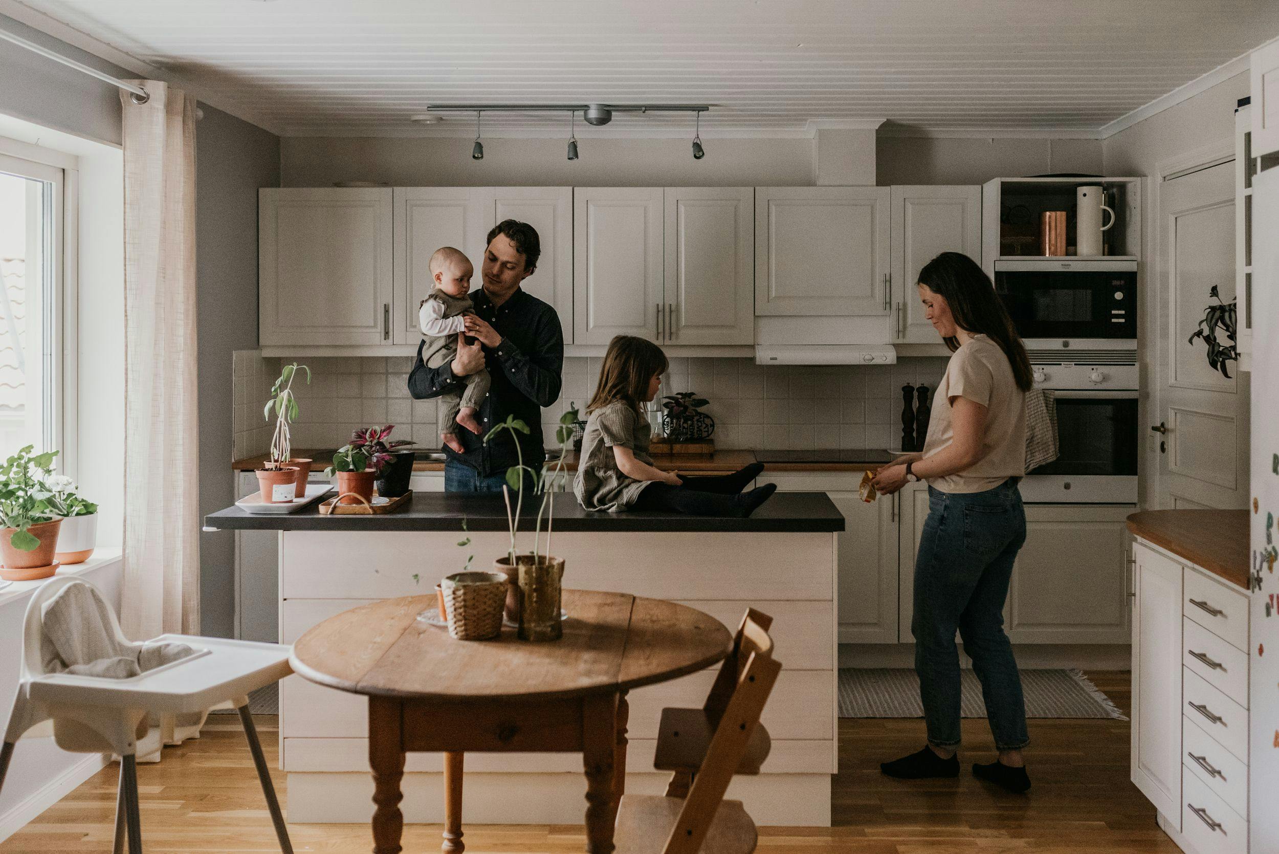 Barnfamilj i vitt kök med ett barn sittandes på köksön